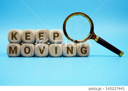 Keep Moving alphabet letters wooden cube and magnifying glass on blue background Keep Moving alphabet letters wooden cube and magnifying glass on blue background 143227441