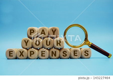 Pay Your Expenses alphabet letters wooden cube and magnifying glass on blue background Pay Your Expenses alphabet letters wooden cube and magnifying glass on blue background 143227464