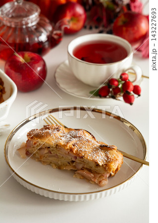 Slice of delicious apple strudel served with hot tea and fresh apples on a white table 143227693