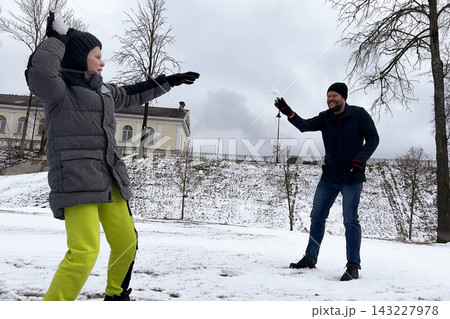 Joyful young boy throwing homemade snowball at his smiling dad inside public city park during winter walk. 143227978