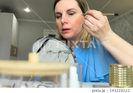 With focused attention, a girl uses the mirror's reflection to guide her hand while applying cosmetics and perfecting her makeup look for the day. With focused attention, a girl uses the mirror's reflection to guide her hand while applying cosmetics and perfecting her makeup look for the day. 143228122