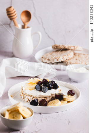 Rice bread with ricotta, banana, and grapes on a plate on the table vertical view Rice bread with ricotta, banana, and grapes on a plate on the table vertical view 143228343