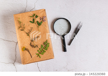 Pressed flowers on a book, a magnifying glass, and tweezers on the table top view Pressed flowers on a book, a magnifying glass, and tweezers on the table top view 143228360