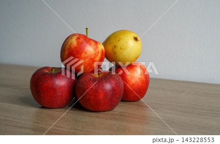 Red apples and a yellow pear are arranged on a wooden table. Concept of fruit, harvest, food, nutrition, abundance, freshness and still life setting 143228553