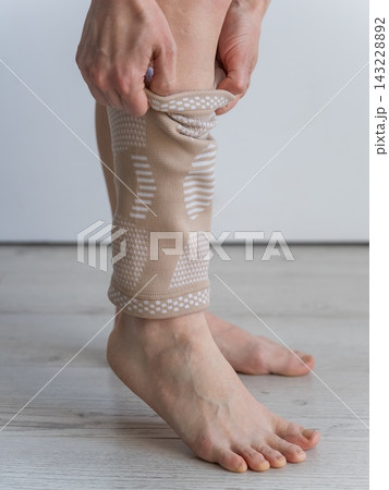 A Caucasian woman suffers from knee pain and wears a supportive elastic knee brace. 143228892