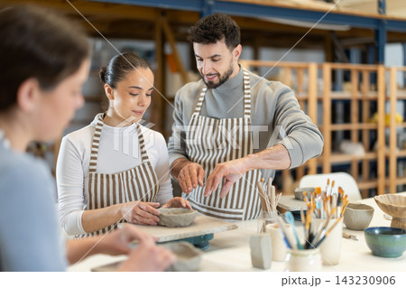 Male master leaned over to girl and helps to sculpting from clay 143230906