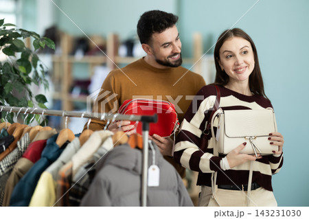 Woman selects handbag in clothing store. Man helps her Woman selects handbag in clothing store. Man helps her 143231030