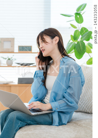 スマホで通話しながらパソコンを使うおしゃれな若いアジア人女性 スマホで通話しながらパソコンを使うおしゃれな若いアジア人女性 143231058
