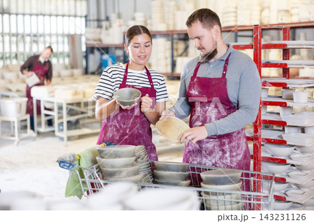Colleagues at ceramic workshop discussing batch of slipcast pottery 143231126