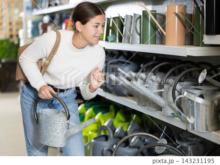 Female customer in hypermarket chooses a garden watering can for her garden Female customer in hypermarket chooses a garden watering can for her garden 143231195