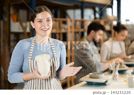 Girl in apron stands with vase in hands, finished clay products from craftsperson 143231220