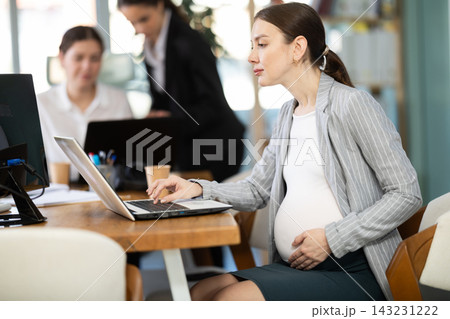 Pregnant woman working on laptop in office Pregnant woman working on laptop in office 143231222