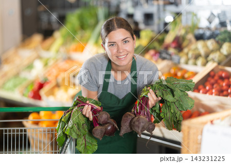 Girl supermarket worker with bunches of beetroots in hands examines product Girl supermarket worker with bunches of beetroots in hands examines product 143231225