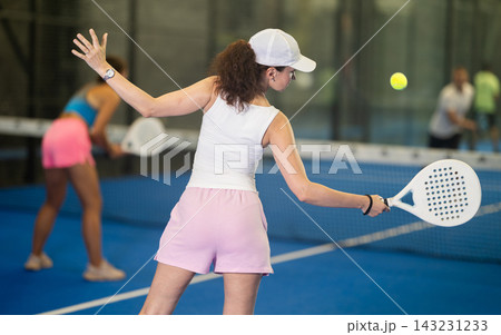 Woman with racket training on outdoor court playing padel game and hitting ball 143231233
