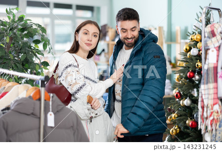Happy couple examine and selecting clothes for cold season in modern store, man trying new coat 143231245