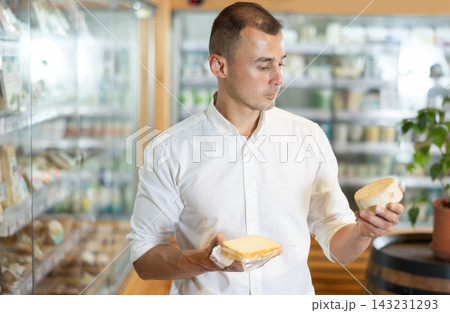 Attentive young man purchaser choosing cheese in large supermarket 143231293