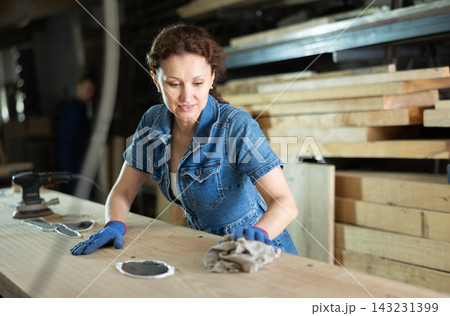 Female sawmill worker cleaning up excess resin or glue on wooden board Female sawmill worker cleaning up excess resin or glue on wooden board 143231399