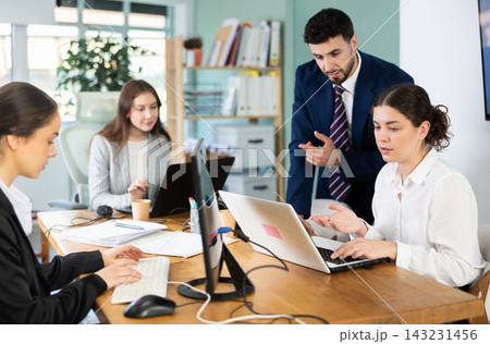 Young man helping female colleague work on laptop Young man helping female colleague work on laptop 143231456