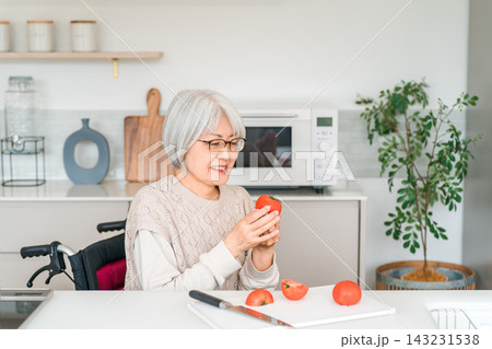 車椅子で料理をするシニア女性。トマトを手に笑顔を見せる健康的な暮らし 143231538