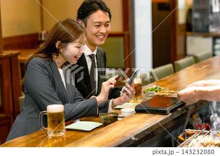 居酒屋でスマホを見ながら食事する男女 143232080