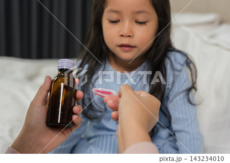 mother feeding liquid medicine to sick preschool child girl with a spoon 143234010