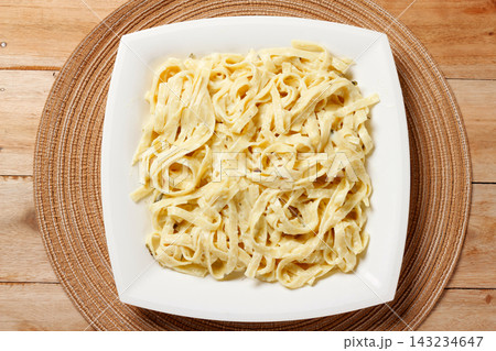 Fettuccine Alfredo with cheese sauce served on a square white plate, garnished with fresh basil, on a wooden table. Fettuccine Alfredo with cheese sauce served on a square white plate, garnished with fresh basil, on a wooden table. 143234647