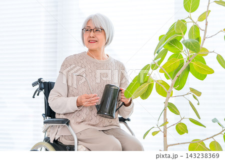 車椅子で観葉植物の世話を楽しむシニア女性。園芸を生きがいにする健康的な老後の暮らし 143238369