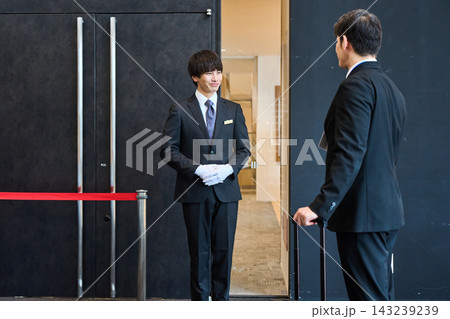 イベント会場の入り口で笑顔でお客様を出迎えるスーツ姿の受付案内スタッフ イベント会場の入り口で笑顔でお客様を出迎えるスーツ姿の受付案内スタッフ 143239239
