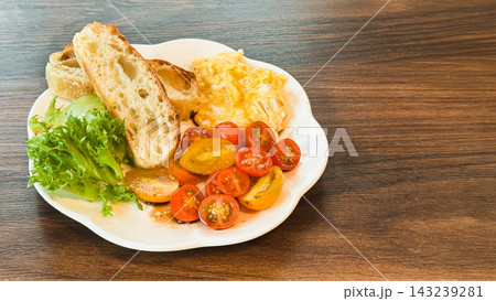 Healthy breakfast with scrambled eggs, toasted, sliced cherry tomato, and fresh greens on wooden surface. 143239281