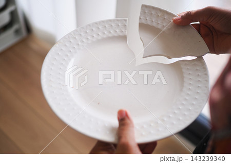 Person holds a broken piece of a plate in a room with wooden flooring Person holds a broken piece of a plate in a room with wooden flooring 143239340