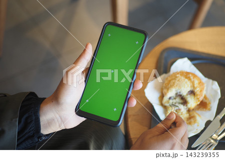 Person using smartphone in cafe while eating cookie Person using smartphone in cafe while eating cookie 143239355