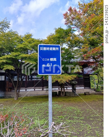 青い災害時避難所と標高表示の案内看板と秋の木々が広がる屋外風景 143239825
