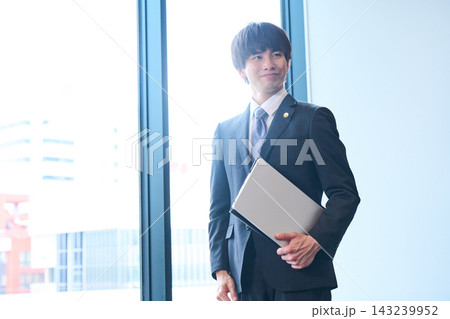窓際でノートPCを手に笑顔を見せるスーツ姿の若い男性士業 窓際でノートPCを手に笑顔を見せるスーツ姿の若い男性士業 143239952