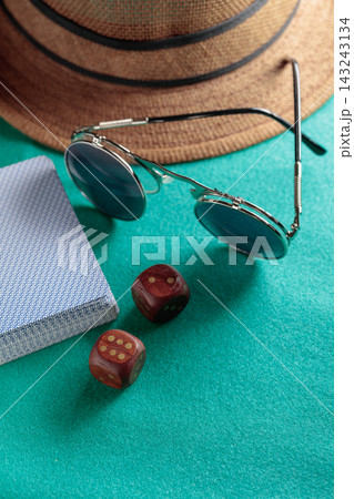 Playing cards, wooden dice, sunglasses and a hat on a green cloth. 143243134