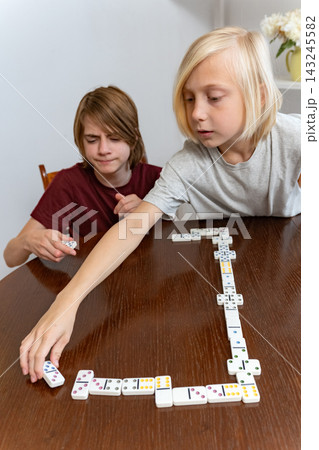 Children playing a game of dominoes at home, concentrating on placing the next tile on the table, enjoying family time and developing cognitive skills 143245582