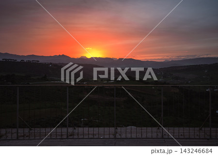 Bright orange sunset over mountains and valley seen through a railing in Ronda Bright orange sunset over mountains and valley seen through a railing in Ronda 143246684