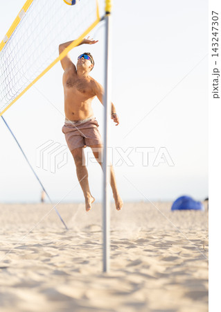 Male athlete spiking volleyball over net on beach Male athlete spiking volleyball over net on beach 143247307