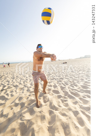 Man playing volleyball on the beach during sunny day near ocean in summer Man playing volleyball on the beach during sunny day near ocean in summer 143247331