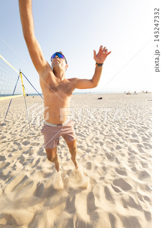Man plays beach volleyball on the sand during sunny day near the ocean 143247332