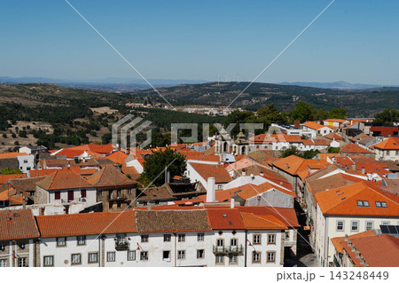 Aerial cityscape of orange tiled rooftops and church bell towers in the old town of Guarda, Portugal, with green hills and wind turbines. Travel and tourism destination in historic Europe. Aerial cityscape of orange tiled rooftops and church bell towers in the old town of Guarda, Portugal, with green hills and wind turbines. Travel and tourism destination in historic Europe. 143248449
