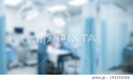 Defocused surgery room interior showing professional surgeons performing medical operation around operating table illuminated by large overhead lamps inside busy clinic department Defocused surgery room interior showing professional surgeons performing medical operation around operating table illuminated by large overhead lamps inside busy clinic department 143250308