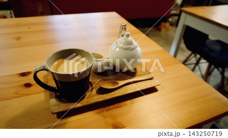 木製テーブルに置かれたコーヒーと白いポットのあるカフェ風景 木製テーブルに置かれたコーヒーと白いポットのあるカフェ風景 143250719
