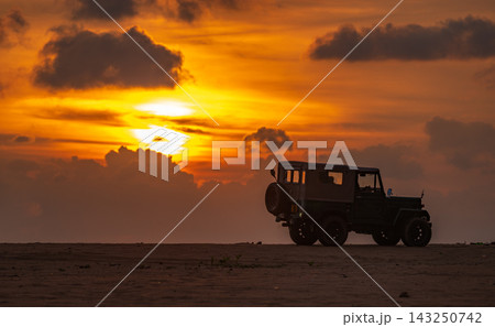 Vintage Off-Road Jeep on the beach, silhouette against a dramatic sunset backdrop Vintage Off-Road Jeep on the beach, silhouette against a dramatic sunset backdrop 143250742