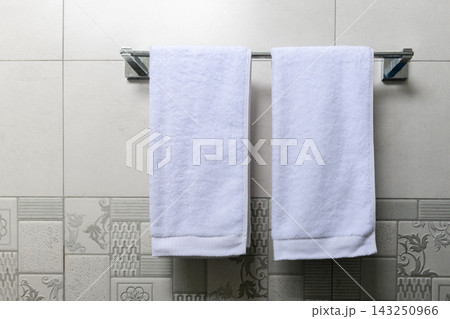 Two clean white towels hang neatly on a towel rack against a tiled bathroom wall Two clean white towels hang neatly on a towel rack against a tiled bathroom wall 143250966