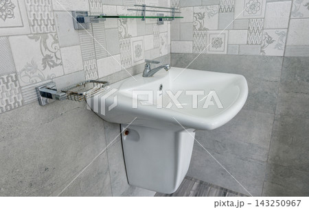 A white ceramic bathroom sink with a chrome faucet and walls with decorative patterned tiles A white ceramic bathroom sink with a chrome faucet and walls with decorative patterned tiles 143250967
