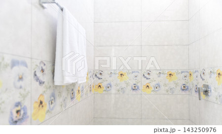 A clean white towel hangs on a towel rack in a tiled bathroom wall A clean white towel hangs on a towel rack in a tiled bathroom wall 143250976