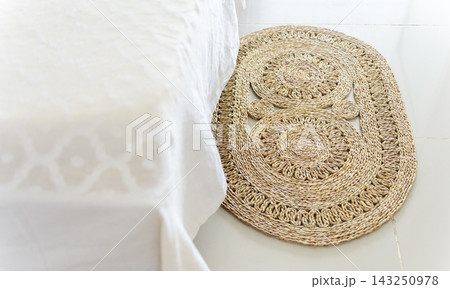 Woven rattan floor mat beside white bed 143250978