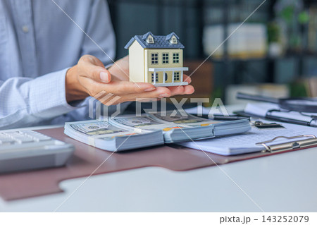 Realtor, home buyer signs a contract of loan approve with cash down payment on table and holding house model 143252079