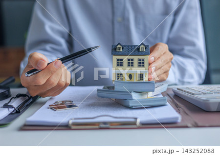 Real estate broker desk with house model, money, and calculator. Mortgage estimation and property purchasing concept. 143252088