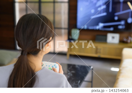 自宅のリビングでゲームコントローラーを持って遊ぶ女性 自宅のリビングでゲームコントローラーを持って遊ぶ女性 143254063